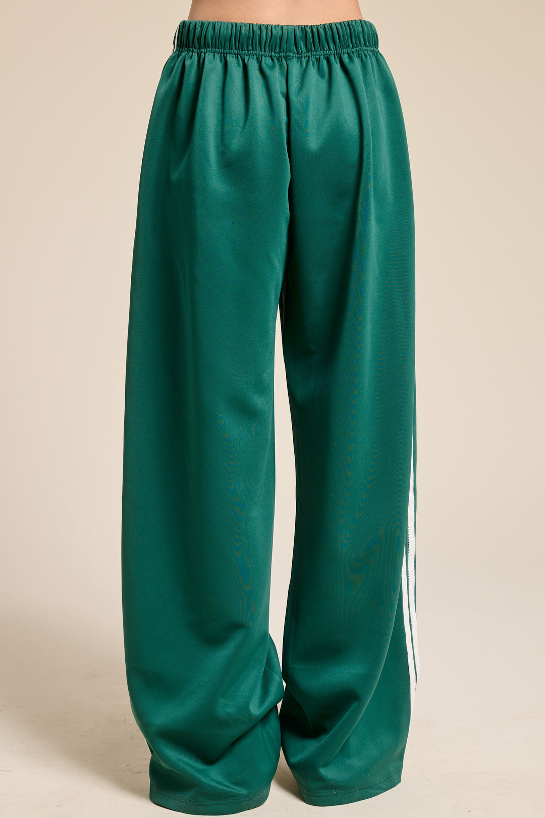Back of person wearing green track pants on plain background