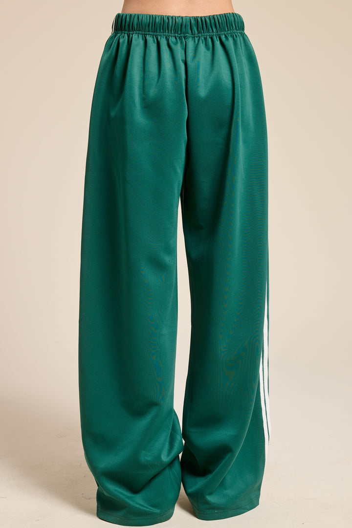 Back of person wearing green track pants on plain background