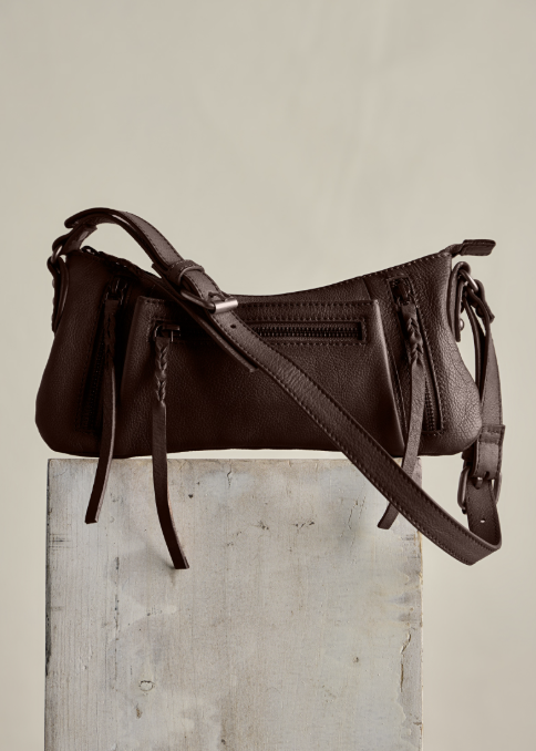 Brown leather crossbody purse on concrete slab and plain background