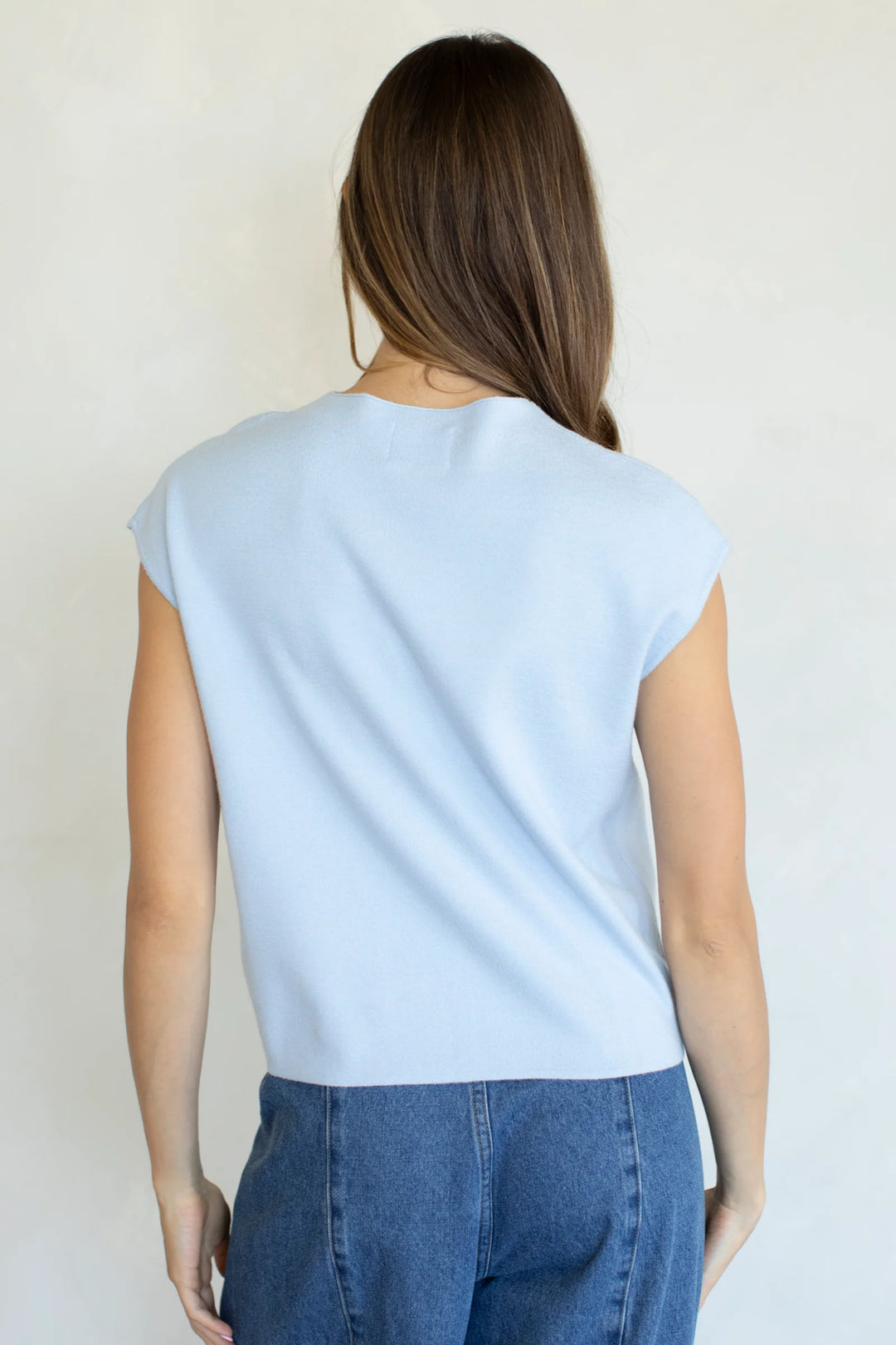 Person wearing a light blue sleeveless top and blue jeans against a plain background