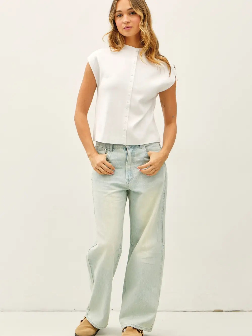 Woman wearing a white sleeveless top and light blue jeans against a white background