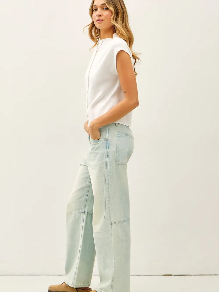 Woman wearing a white sleeveless top and light blue jeans against a white background