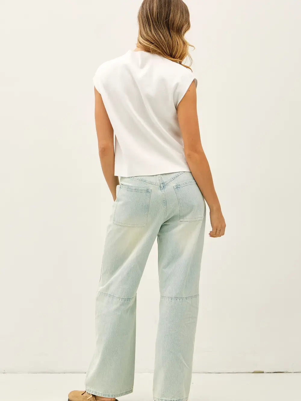 Person wearing light blue jeans and a white sleeveless top on a plain background