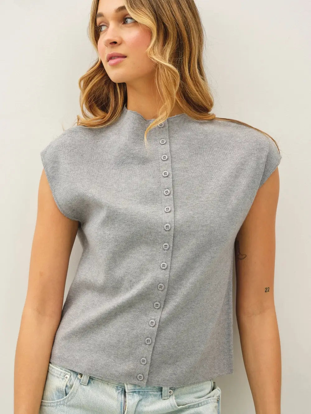 Woman wearing a gray sleeveless top with button details against a plain background