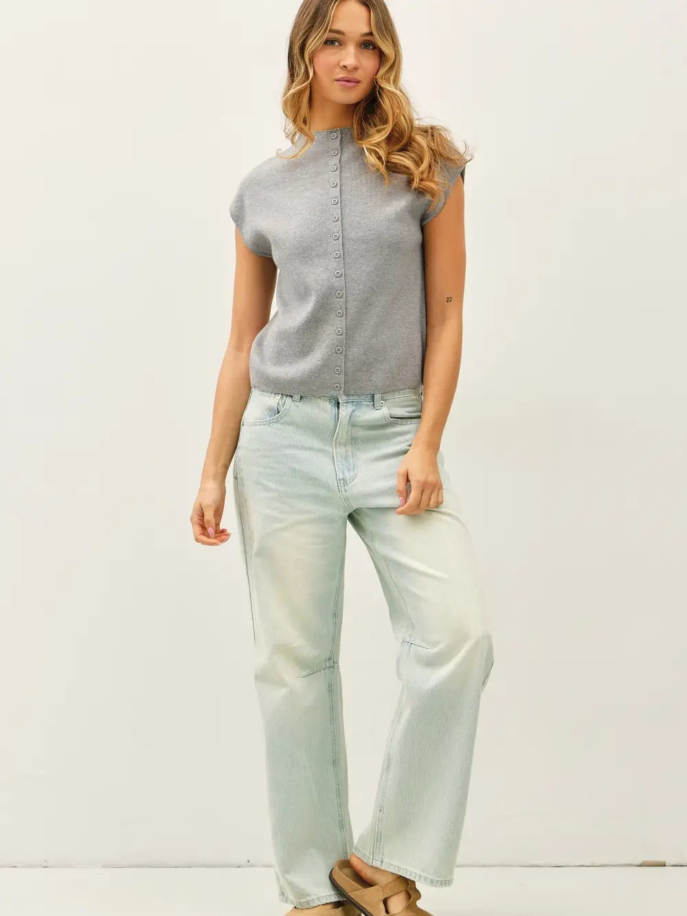 Woman wearing a gray sleeveless top and light blue jeans against a white background