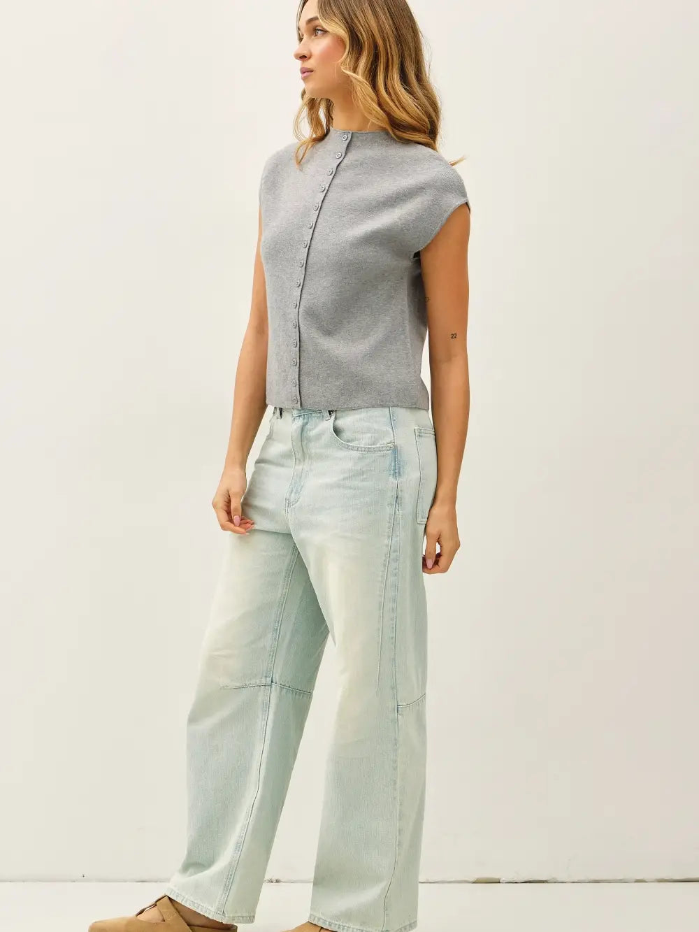 Woman wearing a gray top and light blue jeans against a white background