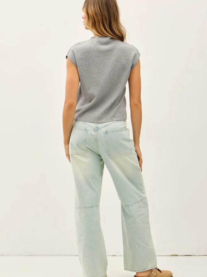 Woman wearing a gray sleeveless top and light blue jeans on a white background