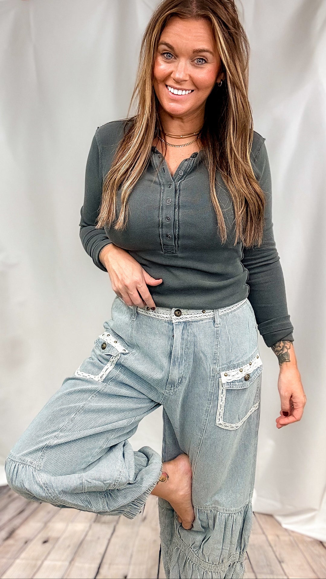 Woman wearing dark grey ribbed henley and striped pants with lace trim on plain background