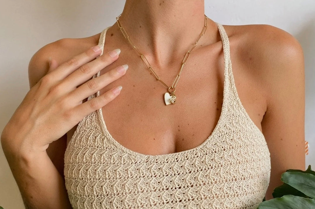 Woman wearing a beige crochet top and gold necklace with a heart pendant.