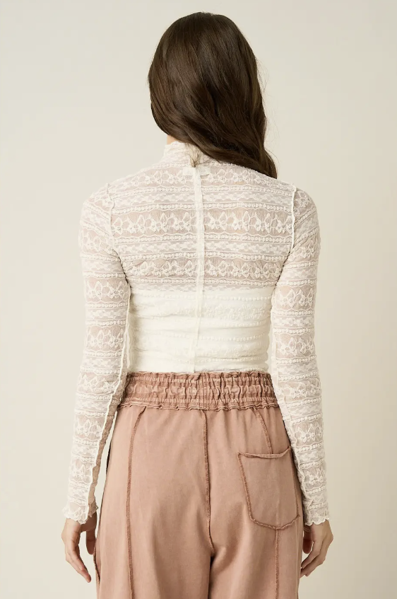 Back of woman wearing lace top and brown pants on plain background
