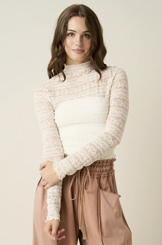 A woman modeling a cream lace mock-neck long-sleeve top paired with dusty rose drawstring pants against a plain beige studio background.