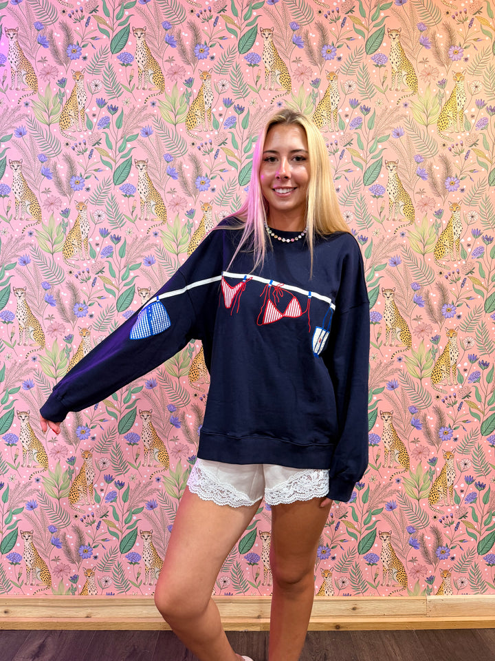Person wearing a navy sweatshirt with colorful accents against a pink patterned wall.