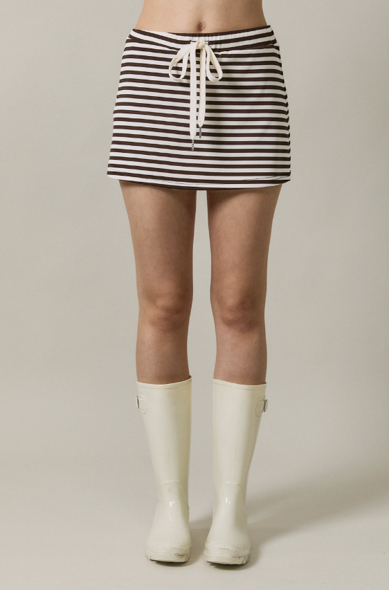 Woman wearing brown and white stripe skirt with white rubber boots on plain background