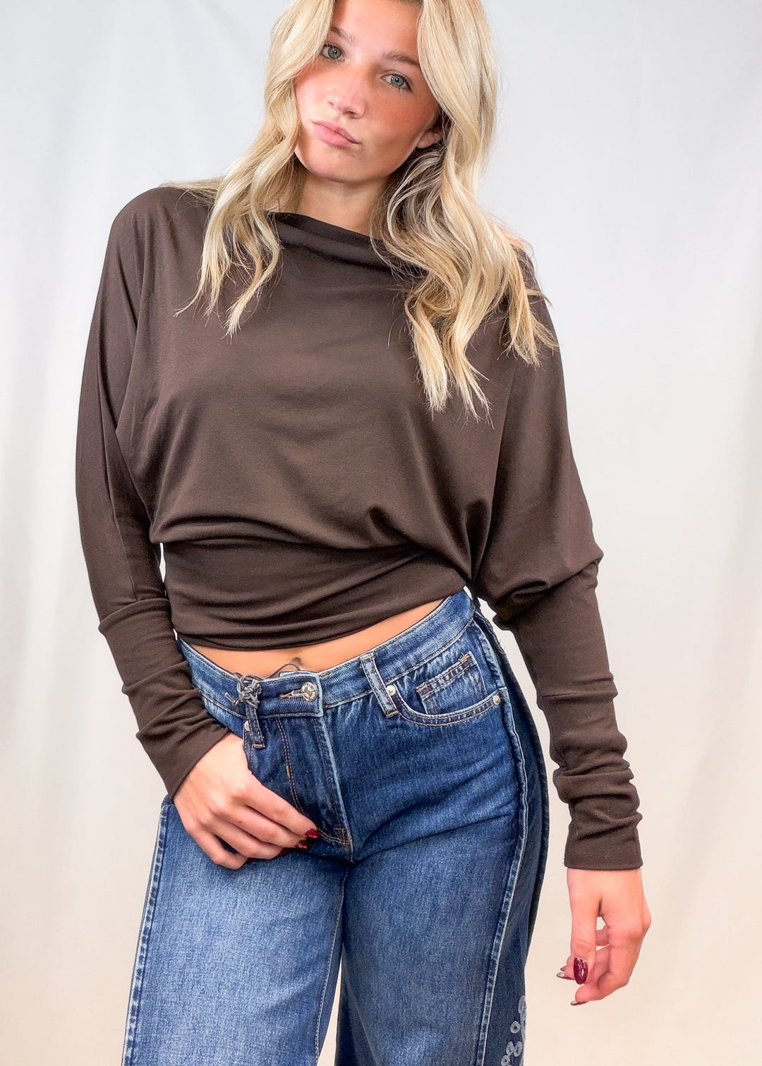 Woman wearing brown long sleeve top with denim jeans on plain background