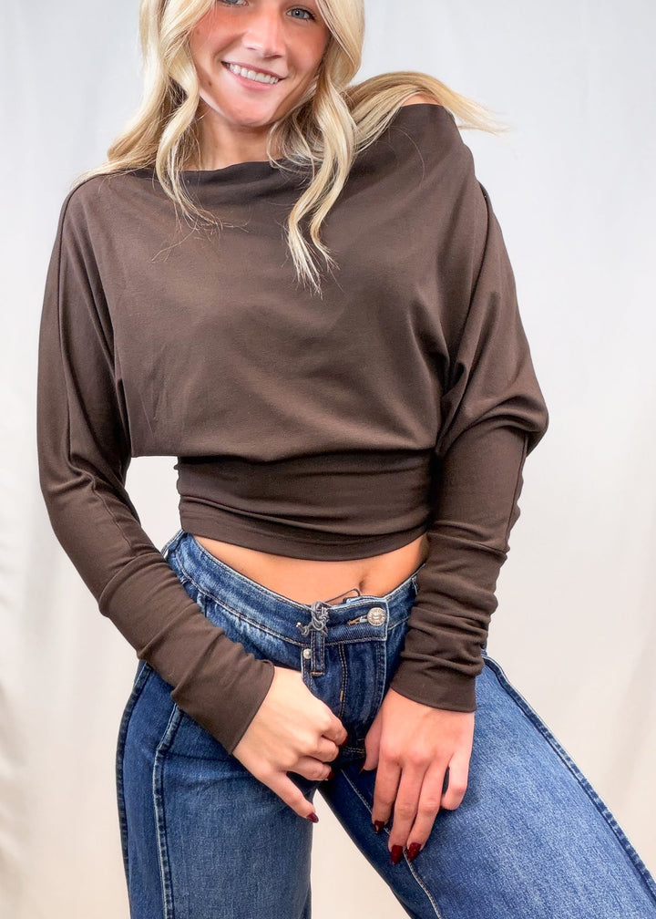 Woman wearing brown long sleeve top with denim jeans on plain background