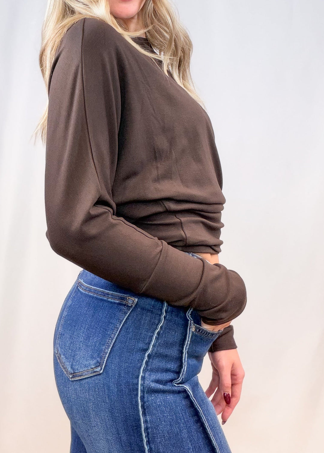 Woman wearing brown long sleeve top with denim jeans on plain background