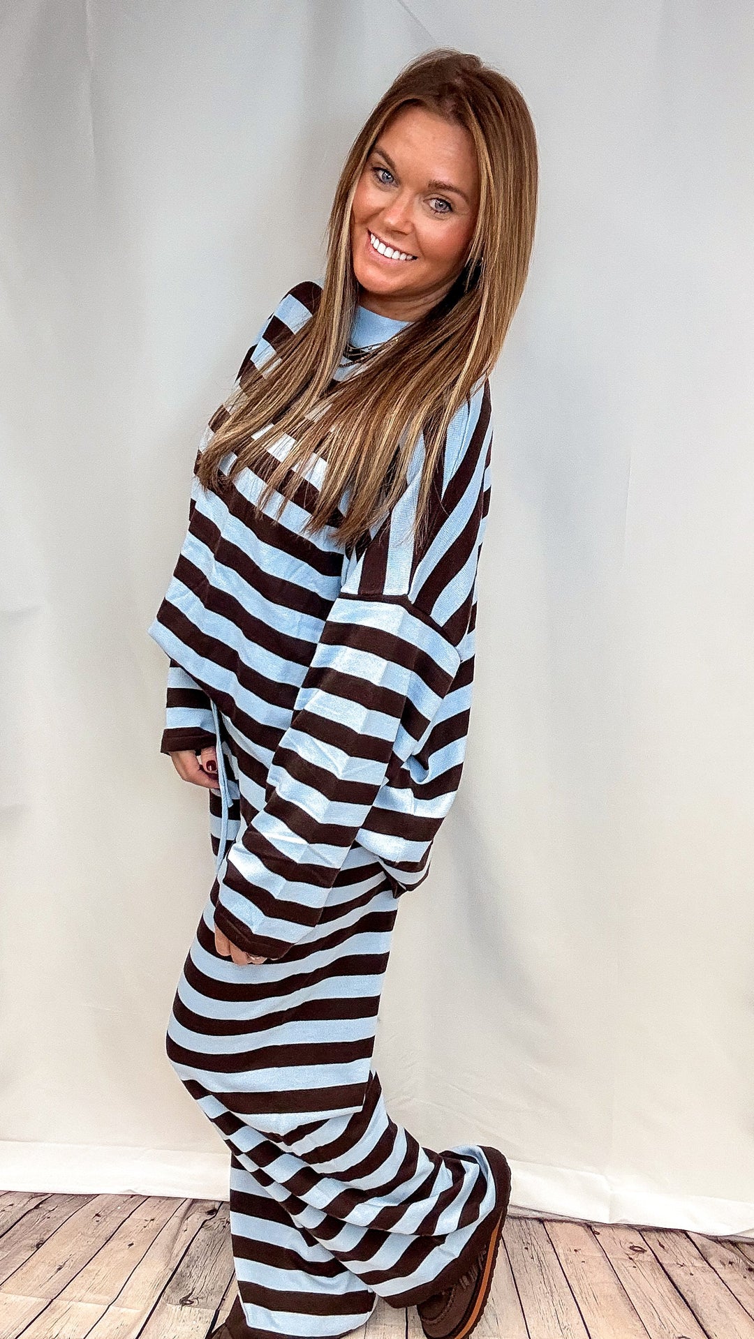 A woman modeling a matching two-piece lounge set with horizontal brown and light blue stripes, standing against a white studio backdrop.