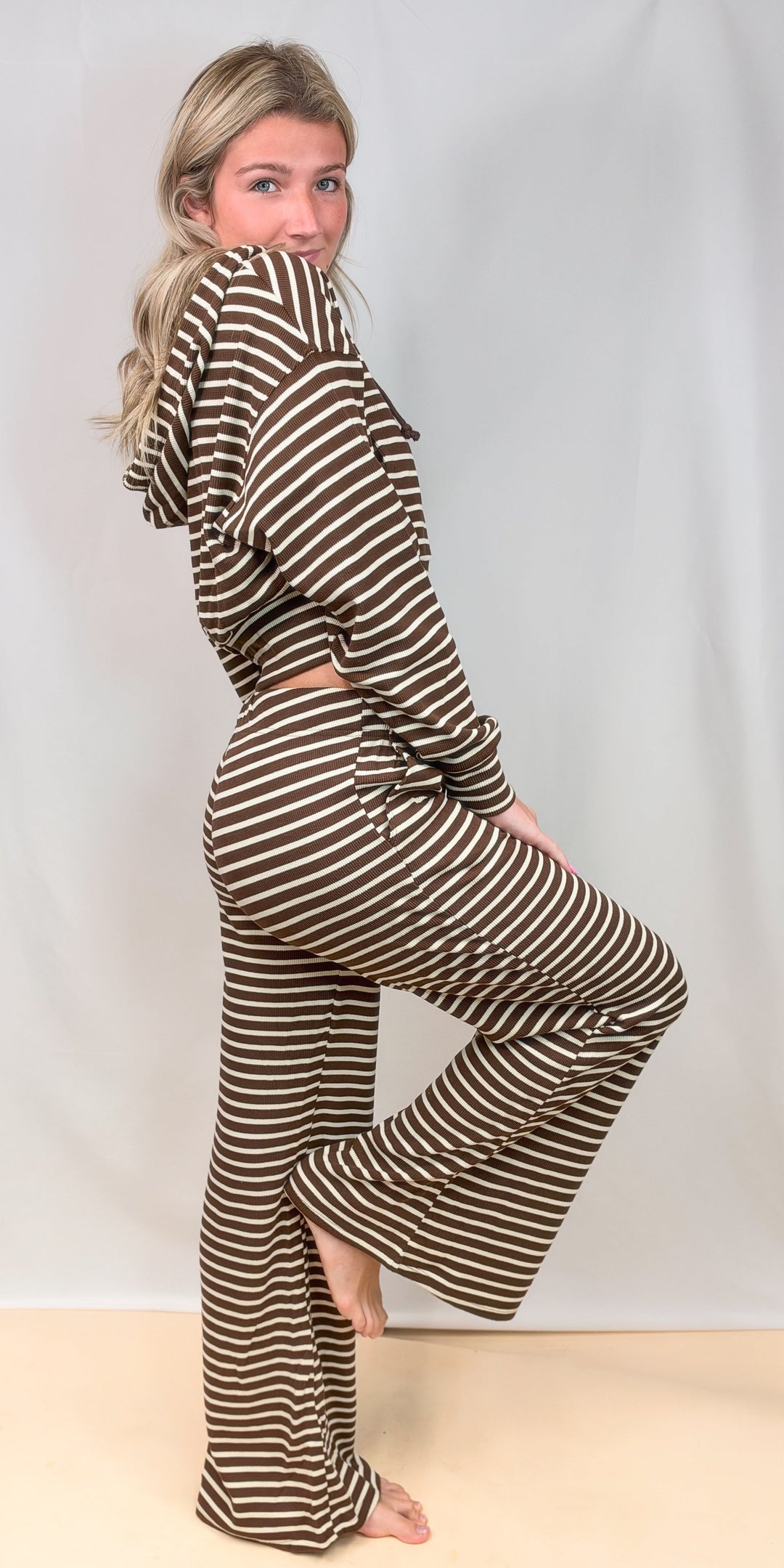 Woman shown from side view wearing brown and white stripe matching set on plain background