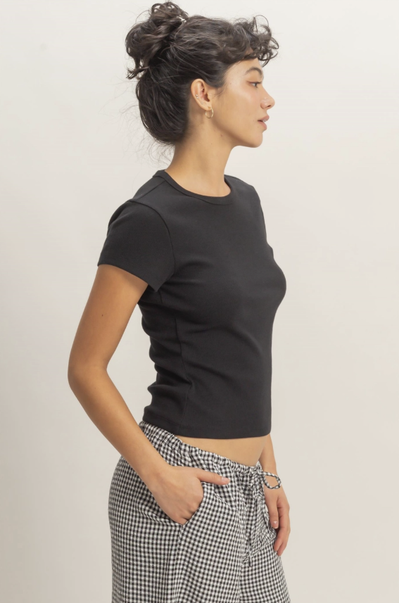 Woman wearing a black crop top and checkered pants against a plain background
