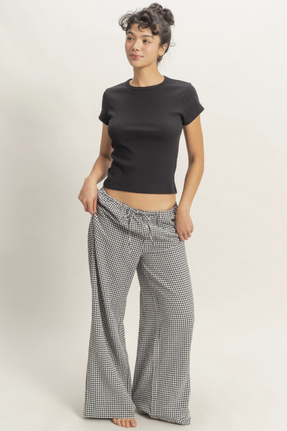 Woman wearing a black top and checkered pants on a plain background