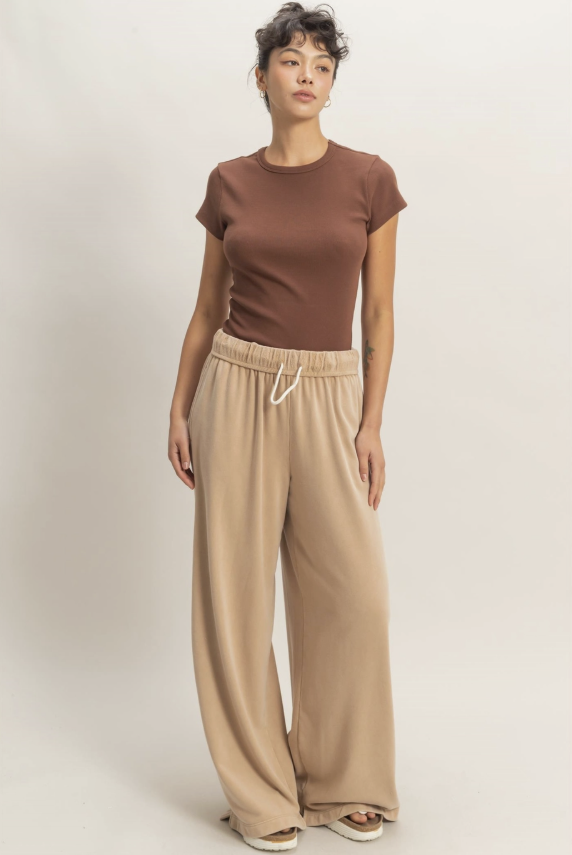 Woman wearing a brown top and beige wide-leg pants on a plain background