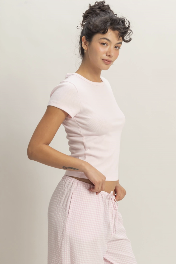 Woman wearing a white t-shirt and light pink checkered pants against a plain background