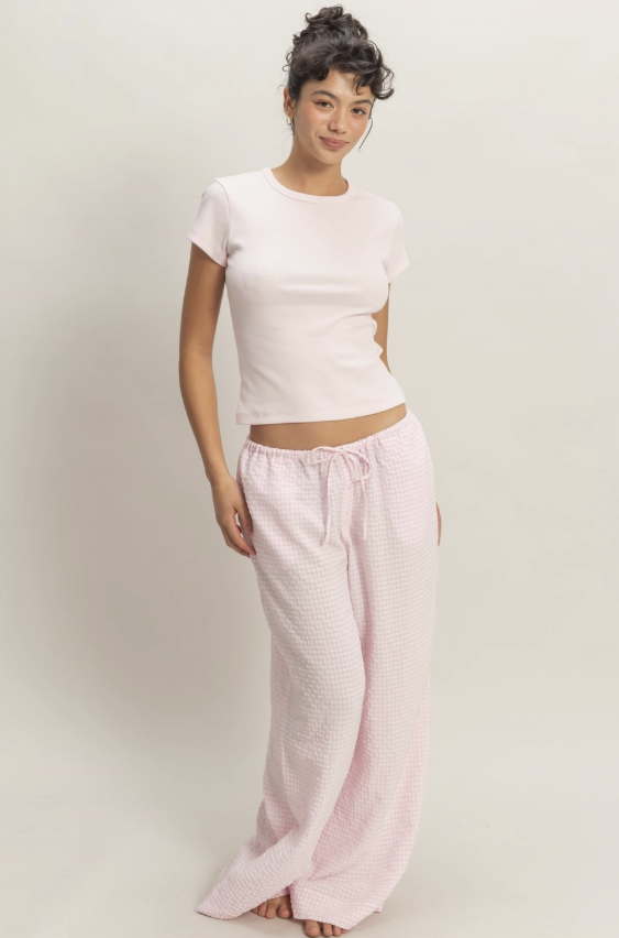 Woman wearing a white top and pink pants on a plain background