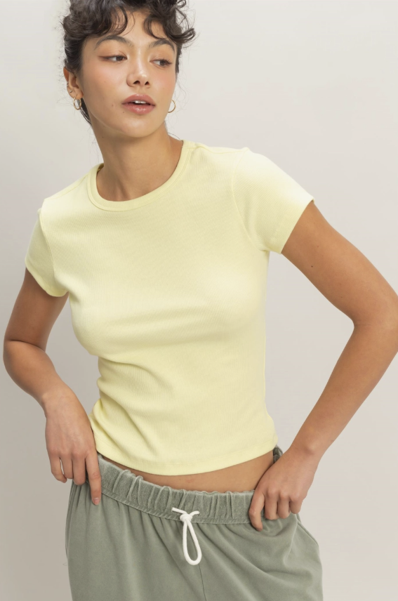 Woman wearing a light yellow t-shirt and gray pants against a plain background