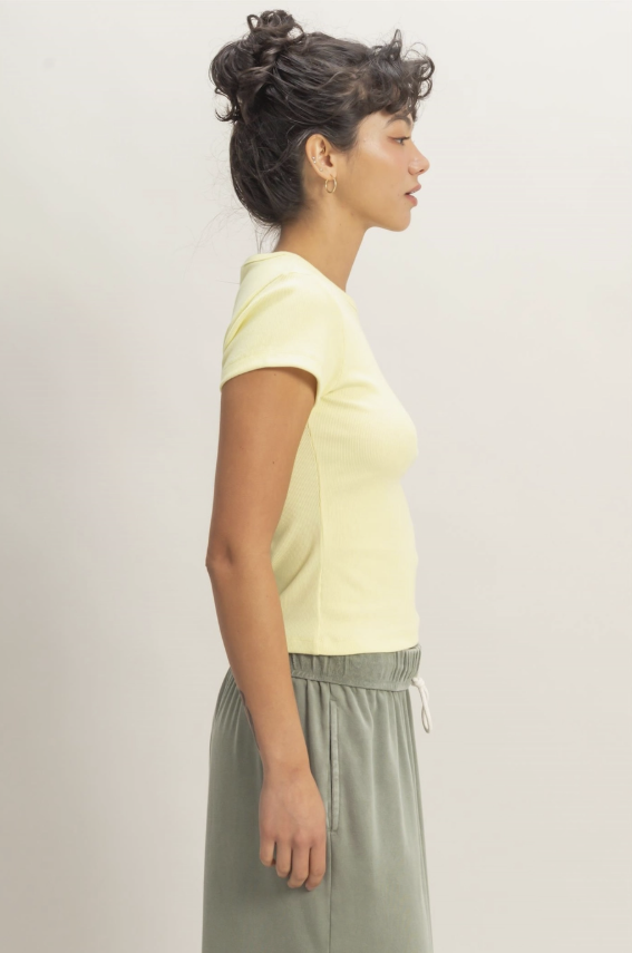 Woman wearing a light yellow top and green pants against a plain background