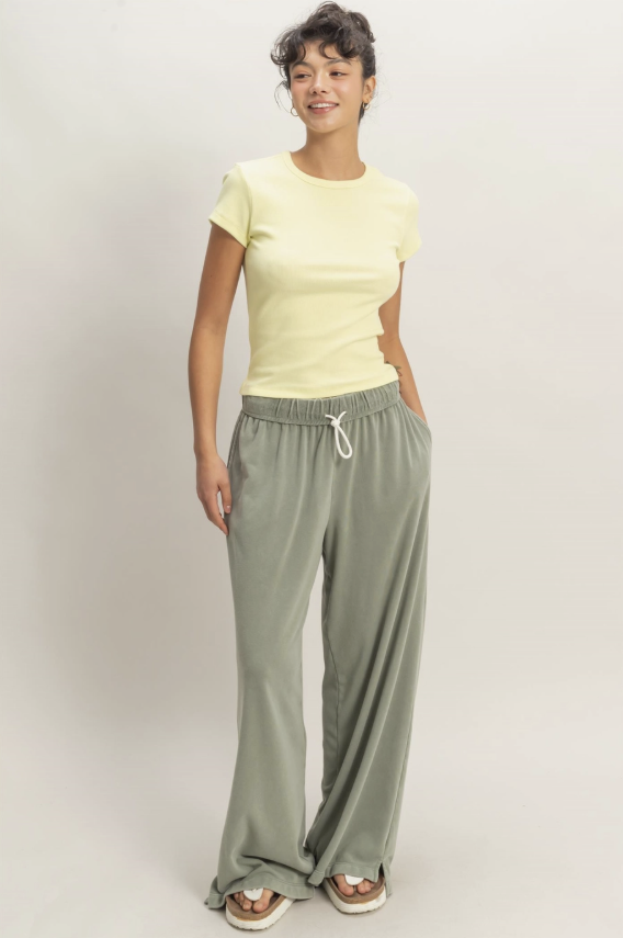 Woman wearing a yellow top and green pants on a plain background
