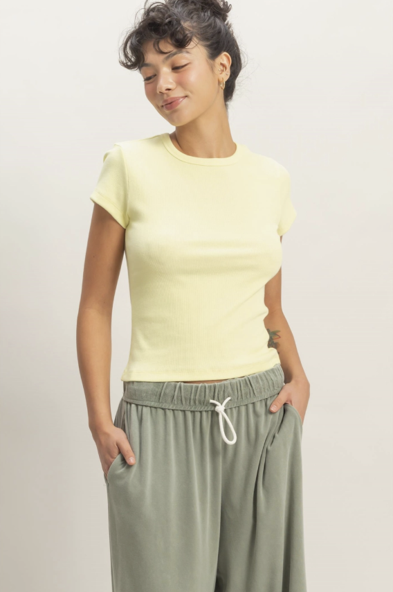 Woman wearing a light yellow top and green pants against a plain background