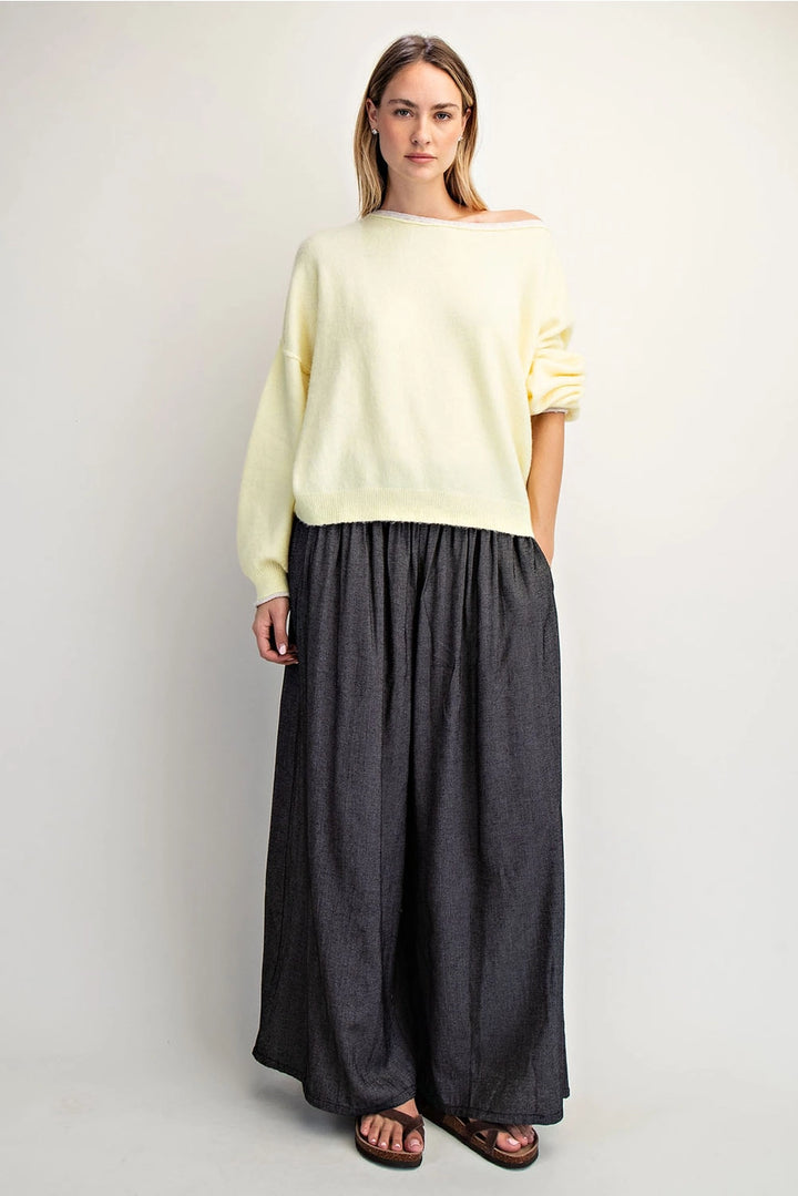 Woman wearing a light yellow sweater and dark gray wide-leg pants on a white background
