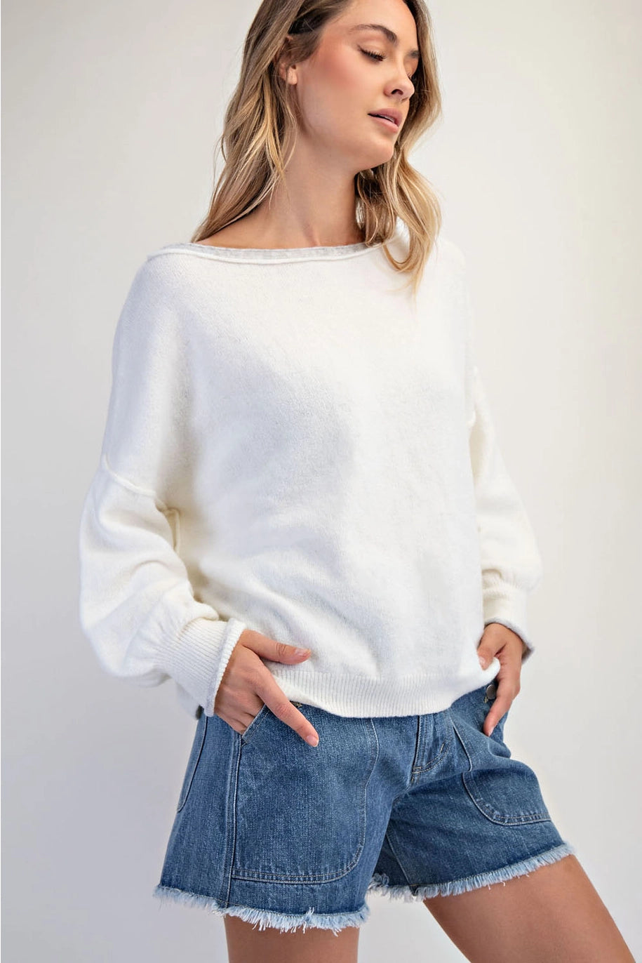 Woman wearing a white sweater and denim shorts on a plain background