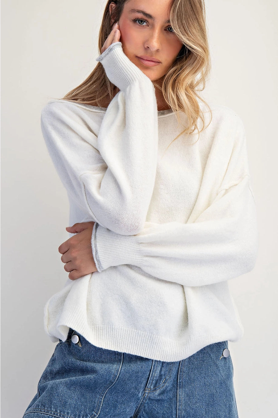 Woman wearing a white sweater and blue jeans on a plain background
