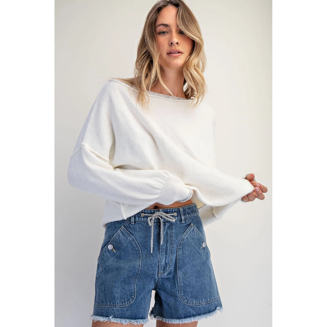 Woman wearing a white sweater and blue denim shorts on a plain background
