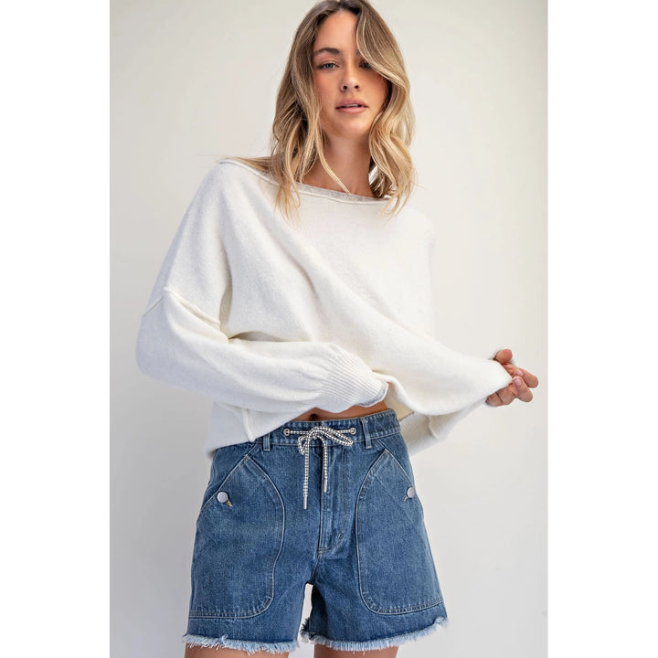 Woman wearing a white sweater and blue denim shorts on a plain background