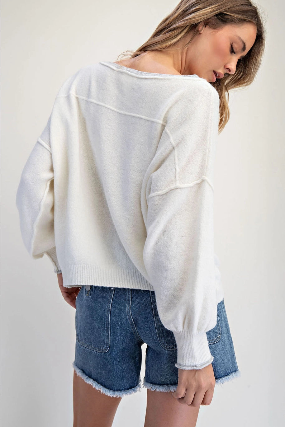 Woman wearing a white oversized sweater and denim shorts on a plain background