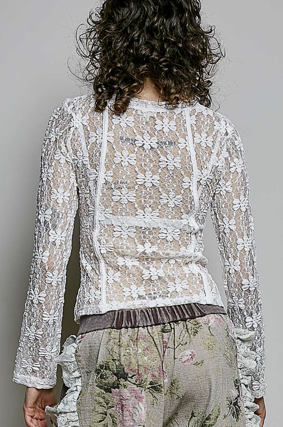 A woman shown from the back wearing a sheer white floral lace long-sleeve top over a beige floral print skirt, against a plain gray studio background.