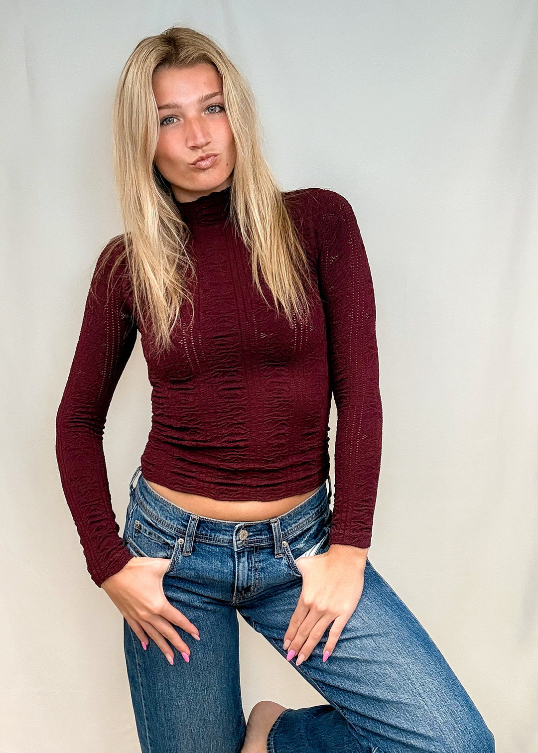 Woman wearing burgundy mock neck top with blue jeans on white background