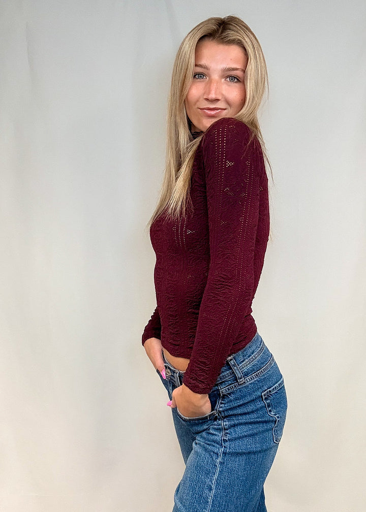 Woman wearing burgundy mock neck top with blue jeans on white background