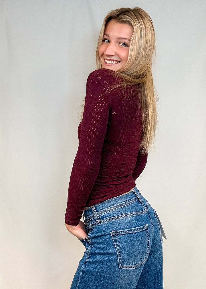 Woman wearing burgundy mock neck top with blue jeans on white background