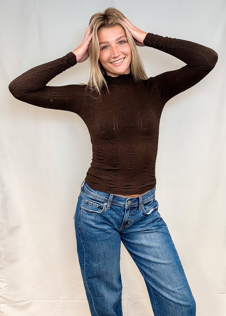 Woman wearing brown mock neck top with blue jeans on white background