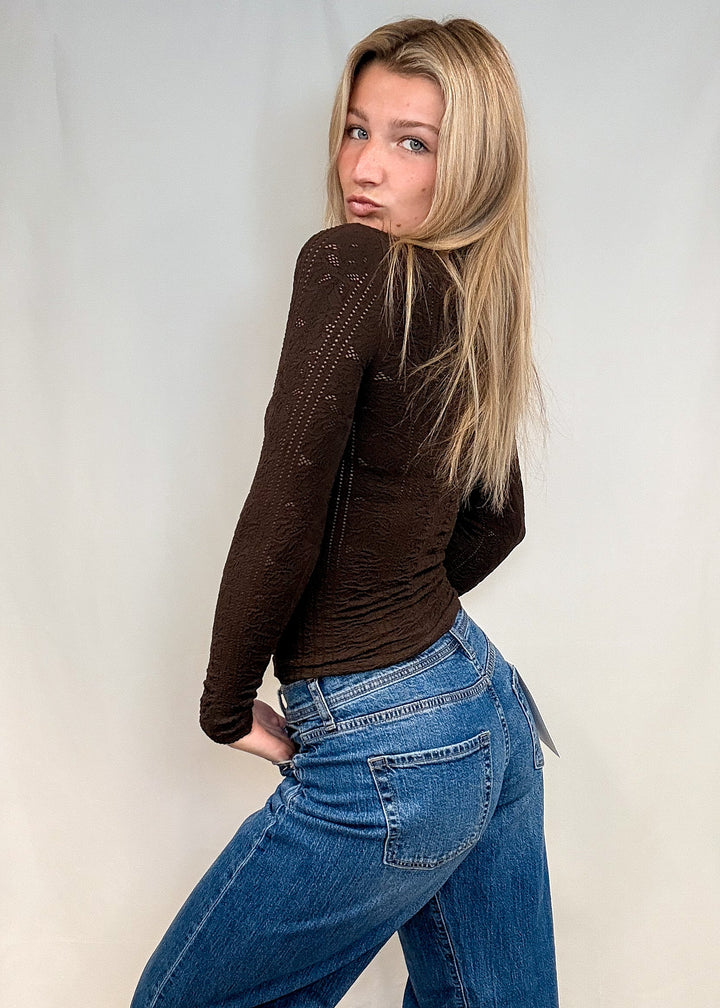 Woman wearing brown mock neck top with blue jeans on white background