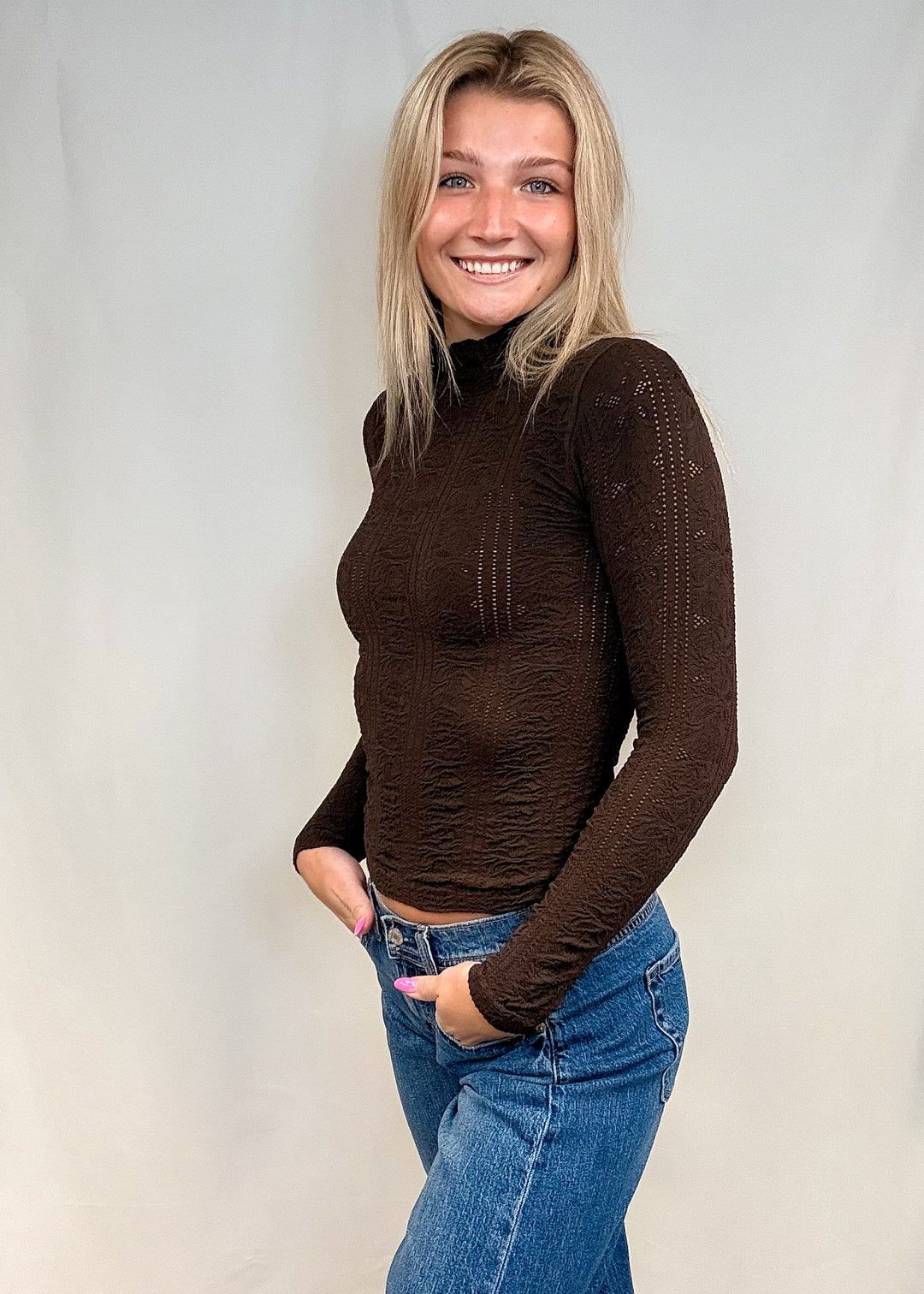 Woman wearing brown mock neck top with blue jeans on white background