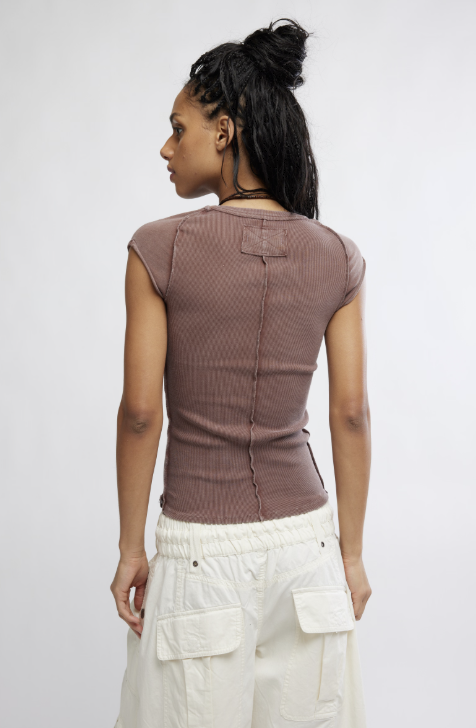 Person wearing a brown ribbed tank top and white pants against a plain background