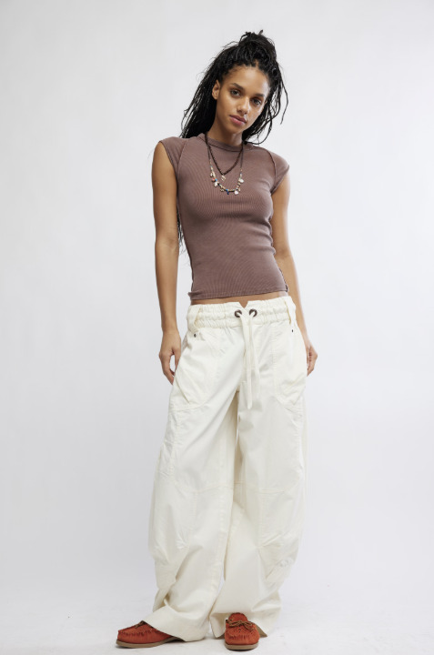 Woman wearing a brown top and white pants on a plain background