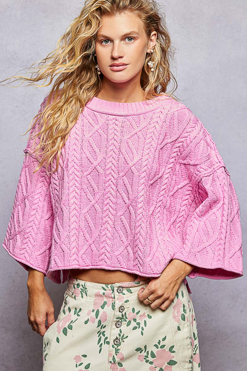 Woman wearing a pink knitted sweater with floral pants against a gray background