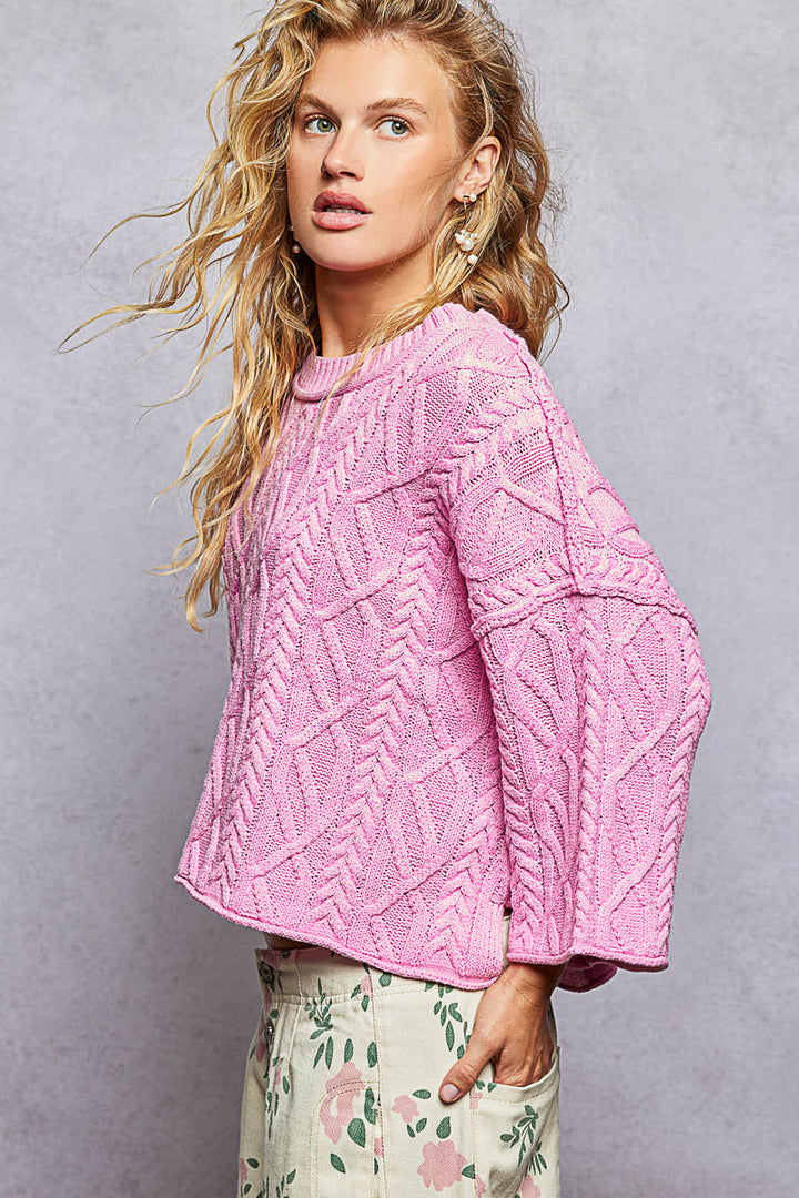 Woman wearing a pink cable knit sweater against a gray background