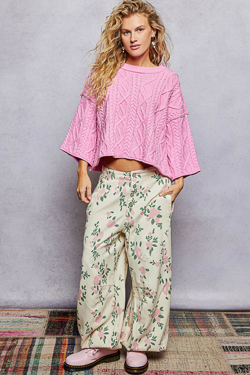 Woman wearing a pink sweater and floral pants against a plain background