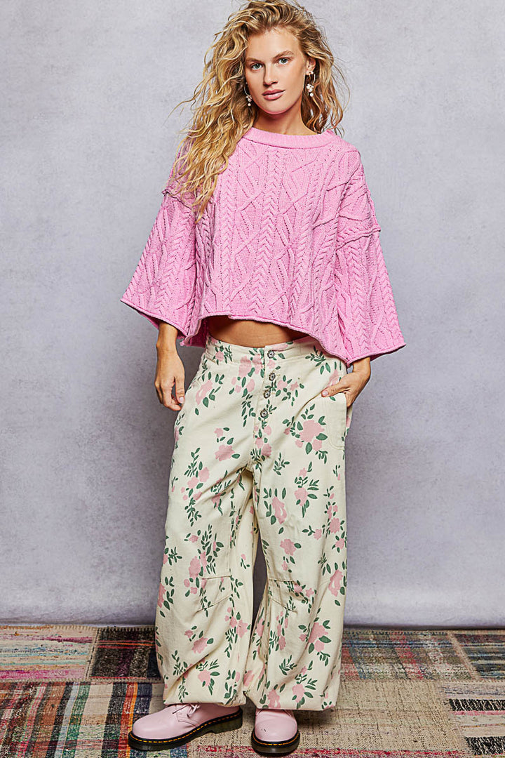 Woman wearing a pink sweater and floral pants against a plain background